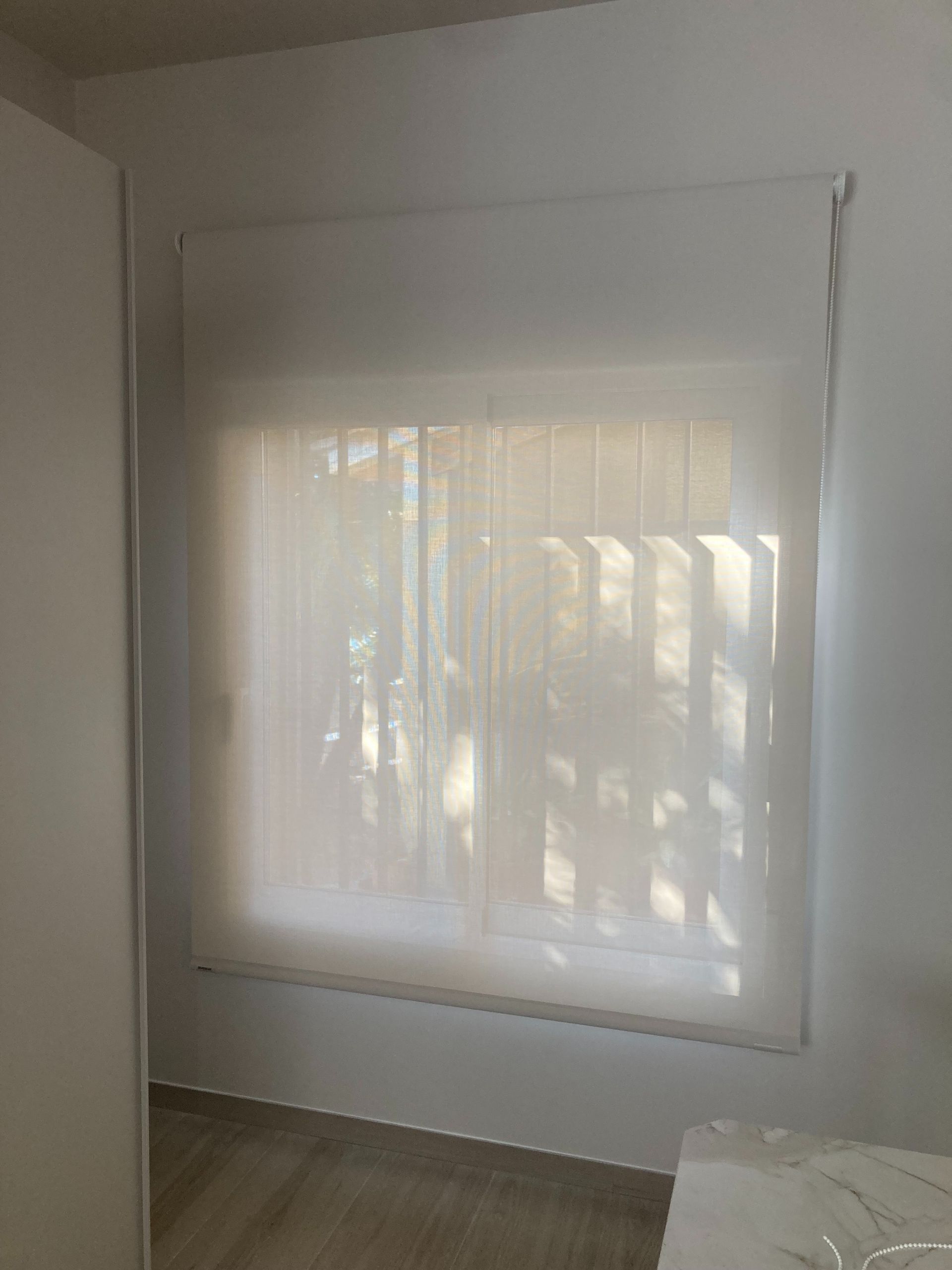 Una persiana blanca está colgada en una ventana de una habitación.