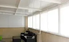 Un solárium con persianas blancas que cubren grandes ventanas, una pared color canela y muebles oscuros.
