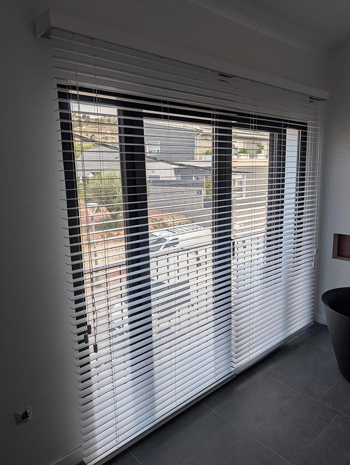 Persianas horizontales blancas que cubren una gran ventana con marcos negros.