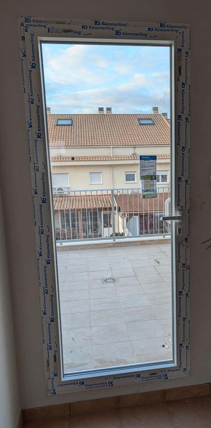 Ventana abierta con marco blanco, vista de edificios y cielo, manija de palanca visible.