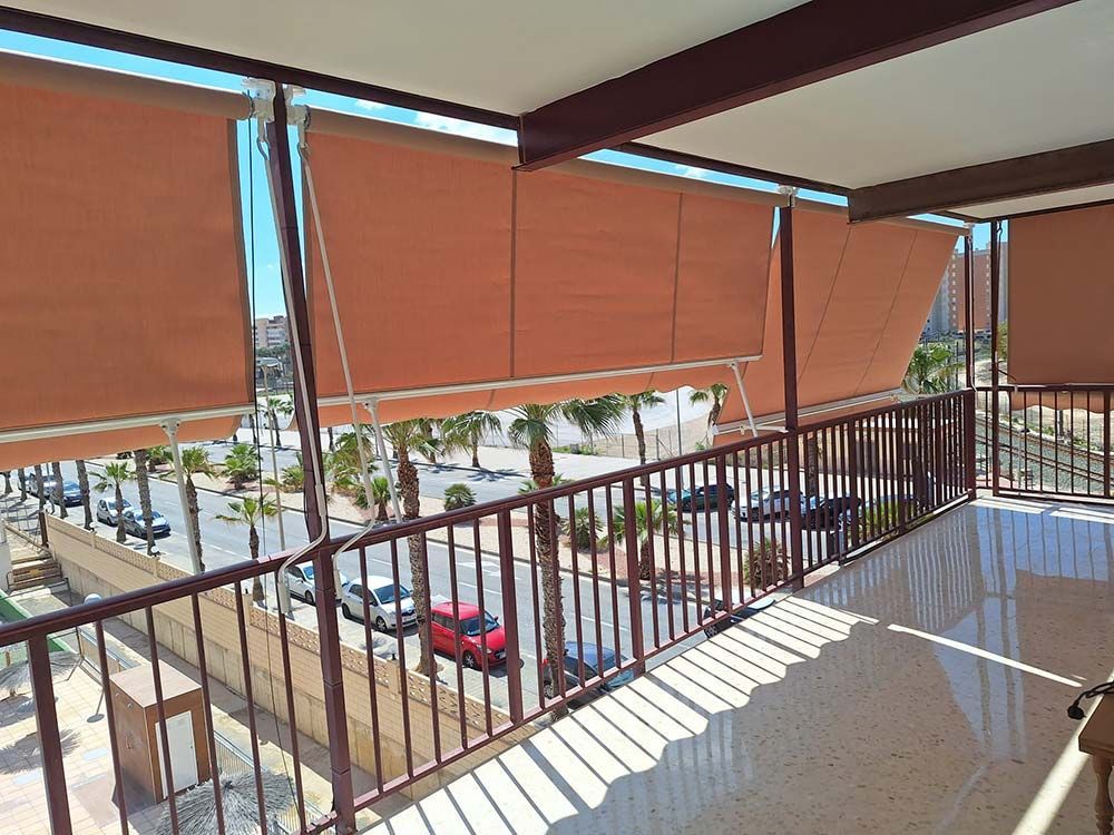 Balcón con tonos beige con vista a calle con autos y palmeras.