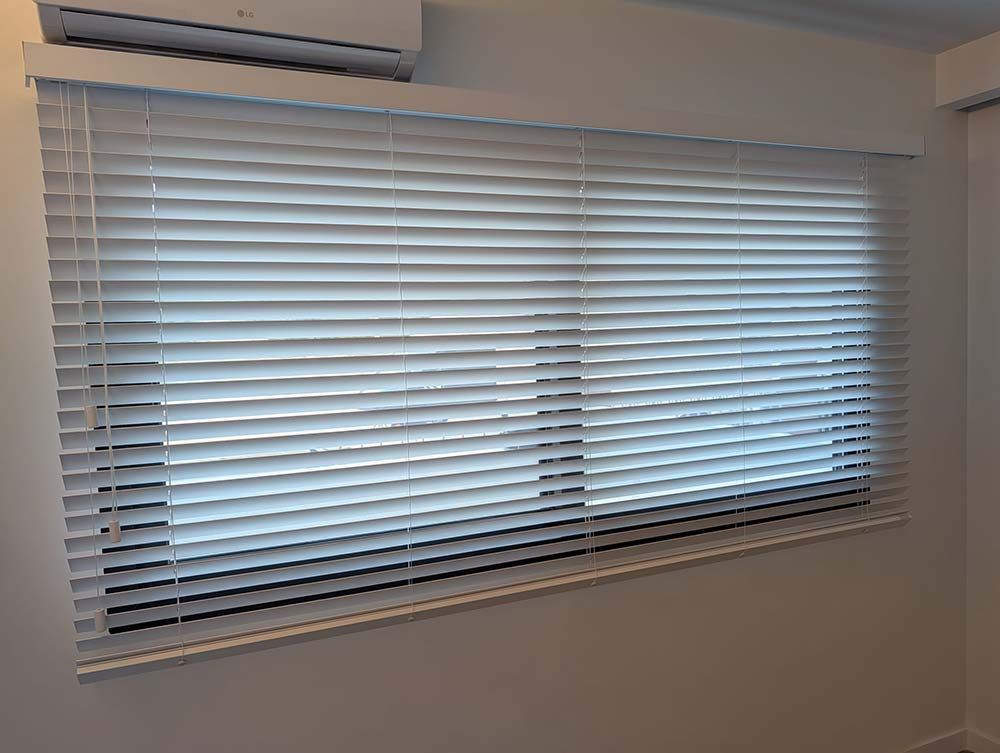 Unas persianas blancas cubren una ventana en una habitación. Hay un aire acondicionado encima.