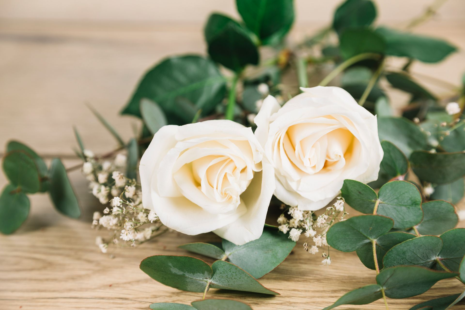 Dos rosas blancas con eucalipto verde y aliento de bebé sobre una superficie de madera.
