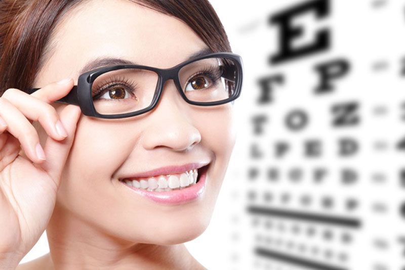 Una mujer que lleva gafas sonríe delante de una tabla optométrica.