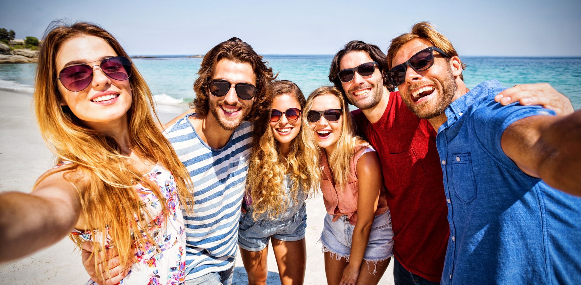 Eine Gruppe junger Leute macht ein Selfie am Strand.