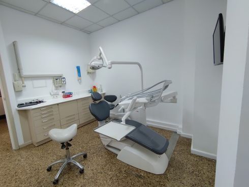 Sala de exploración dental con sillón, armarios y equipos.