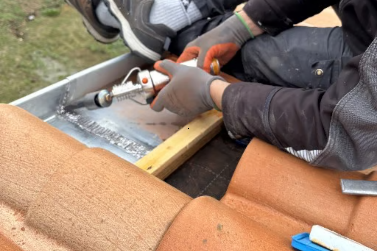 Une personne soude des solins métalliques sur un toit de tuiles, portant des gants.