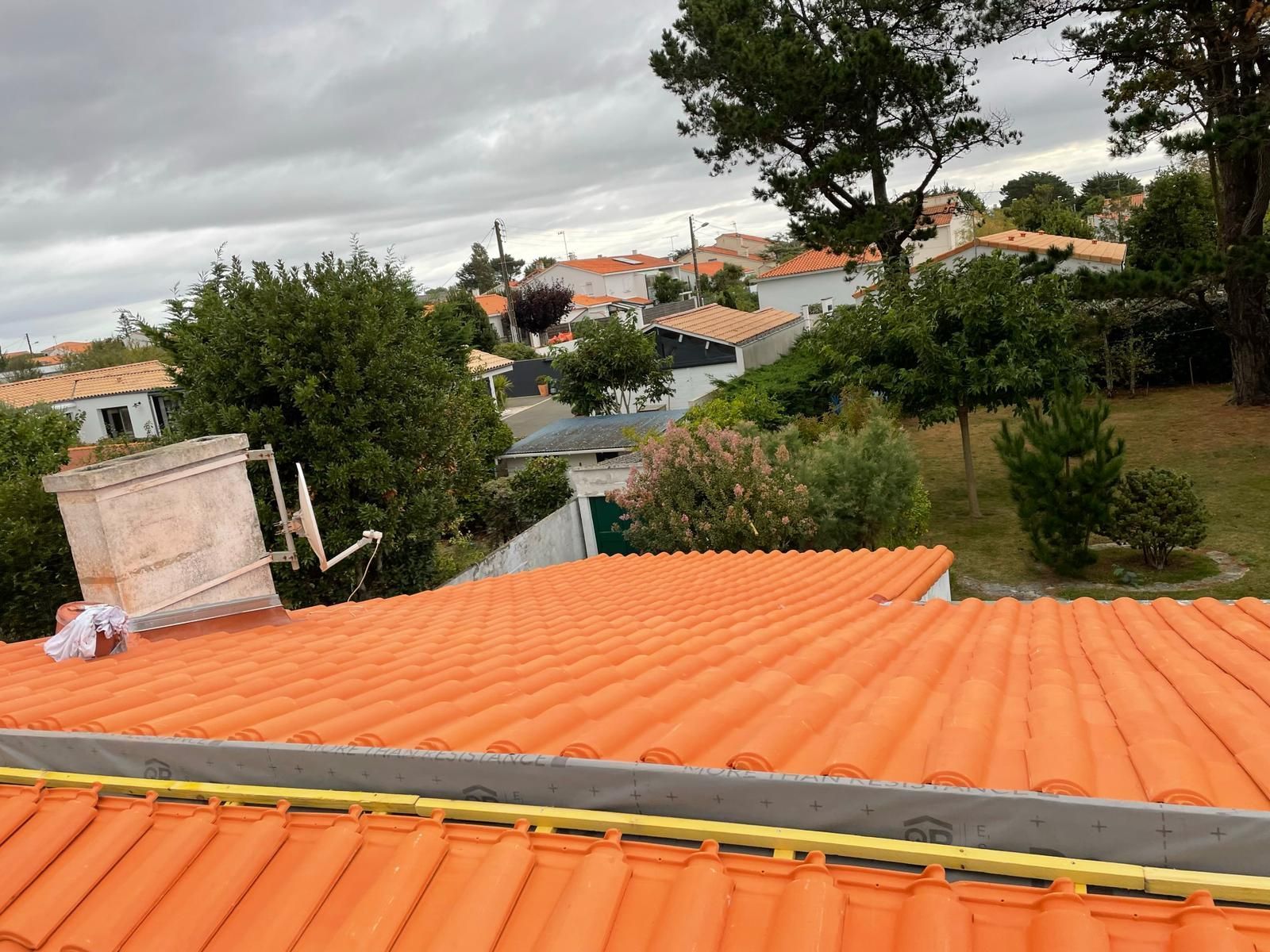 Une personne portant des gants place des tuiles de toit en terre cuite sur une charpente en bois.