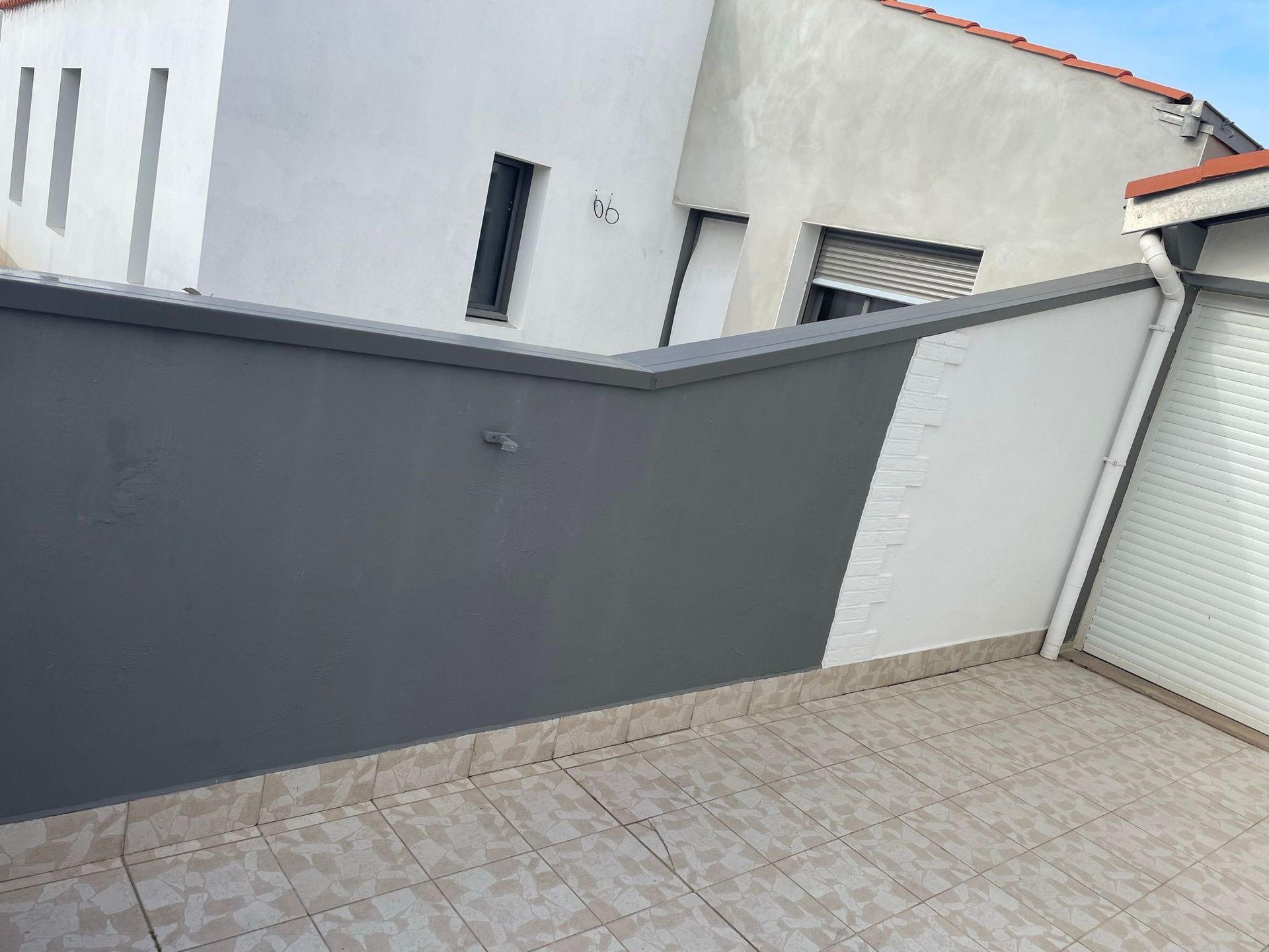 Une personne peint en blanc le côté d'une maison, debout sur une échelle en plein jour.