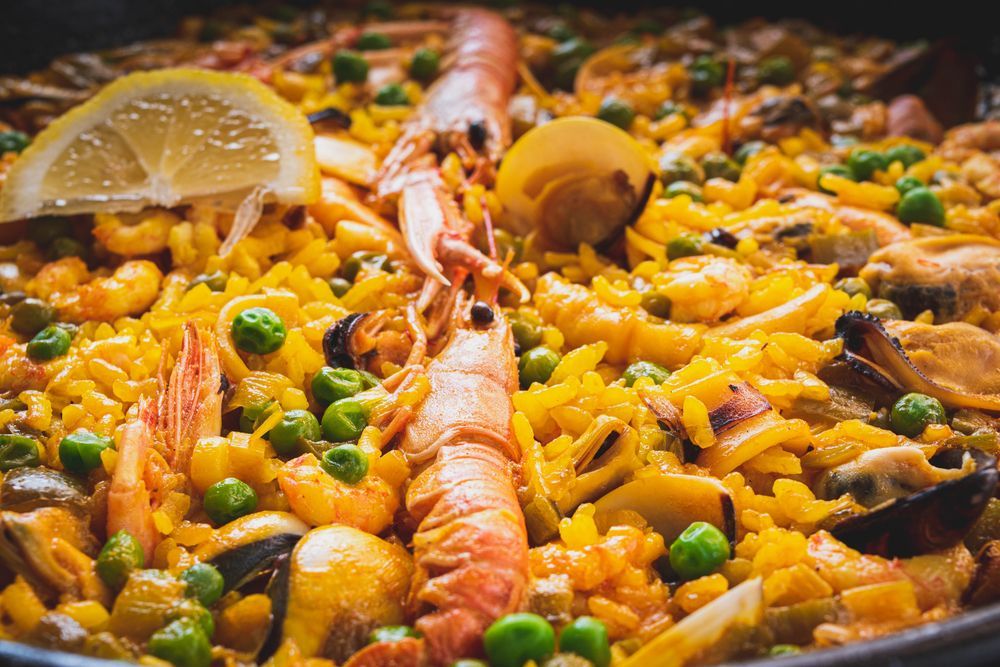 Un primer plano de una paella con camarones, guisantes, champiñones y rodajas de limón.