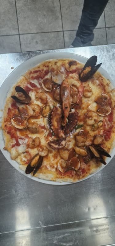 Una pizza con mariscos está en un plato sobre una mesa.