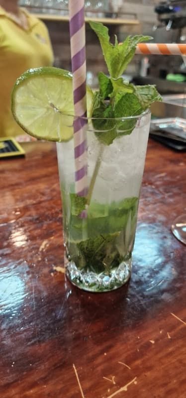 Un vaso de mojito con una pajita y una rodaja de lima sobre una mesa de madera.