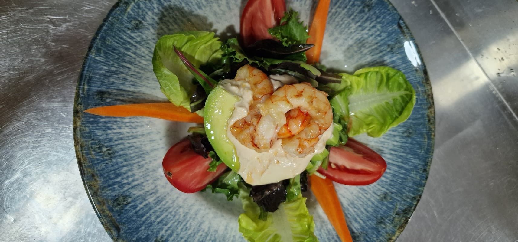Una ensalada con camarones, tomates, lechuga y zanahorias en un plato sobre una mesa.