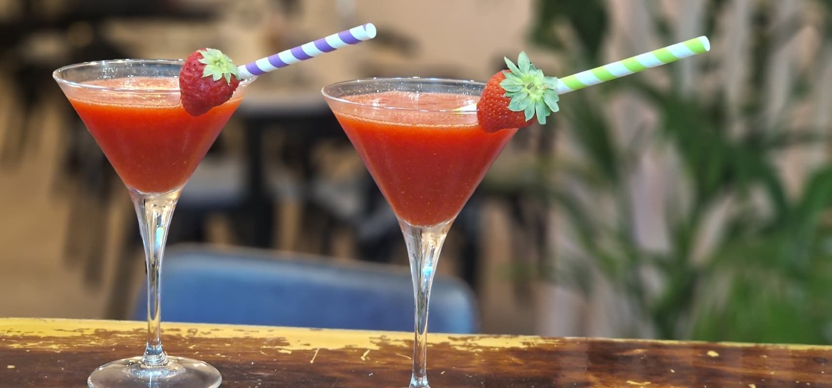 Dos copas de martini llenas de líquido rojo y fresas sobre una mesa.