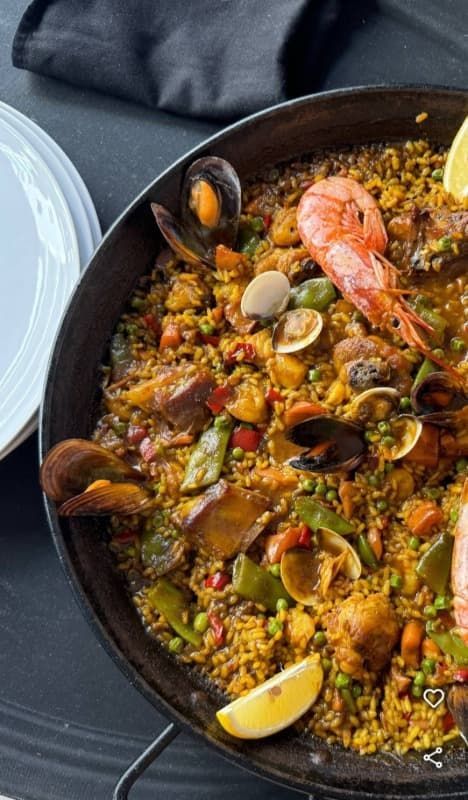 Una sartén de paella con camarones, mejillones y verduras sobre una mesa.