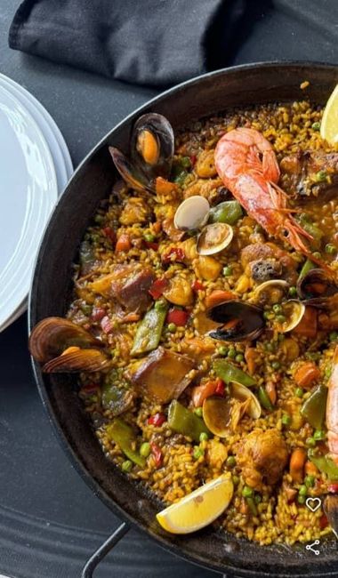Un primer plano de una paella con camarones, guisantes, champiñones y rodajas de limón.