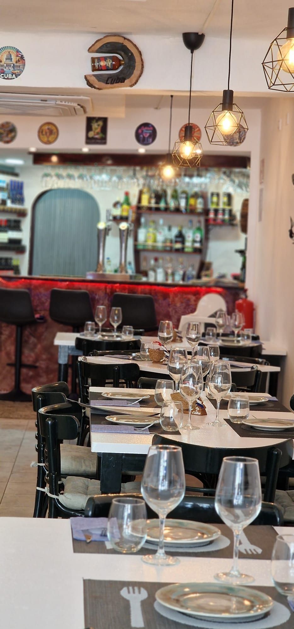 Interior de restaurante con mesas dispuestas para cenar y un bar al fondo.