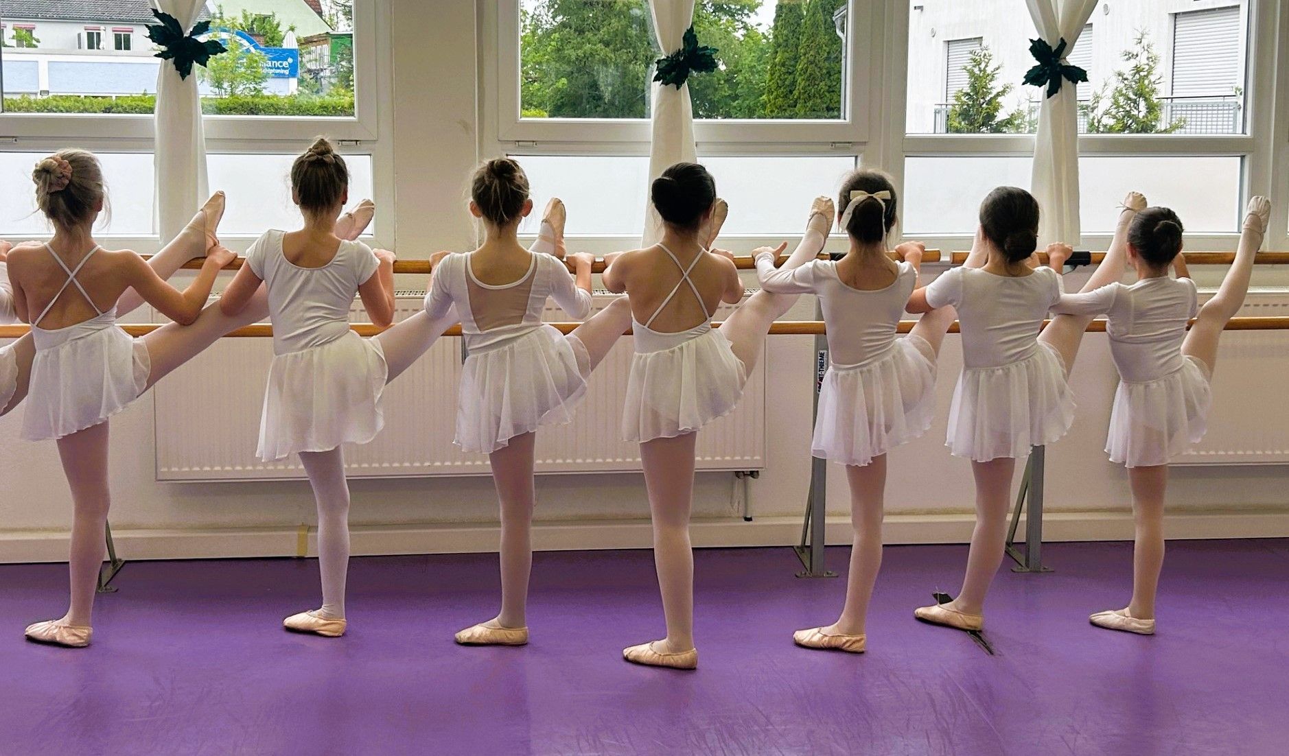 vier Mädchen in kniender Ballettposition mit pinkfarbenen Tutus und Ballettlehrerin