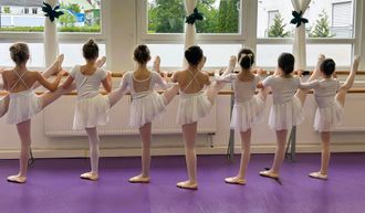 vier Mädchen in kniender Ballettposition mit pinkfarbenen Tutus und Ballettlehrerin