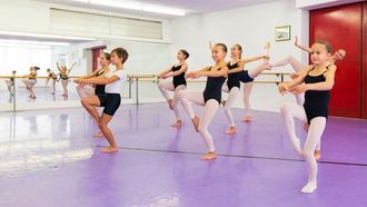 vier Mädchen in kniender Ballettposition mit pinkfarbenen Tutus und Ballettlehrerin
