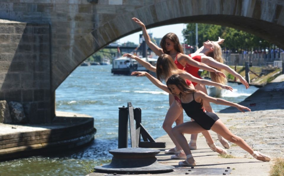 Balletttänzerinnen vor einer Wasserfläche und Brücke