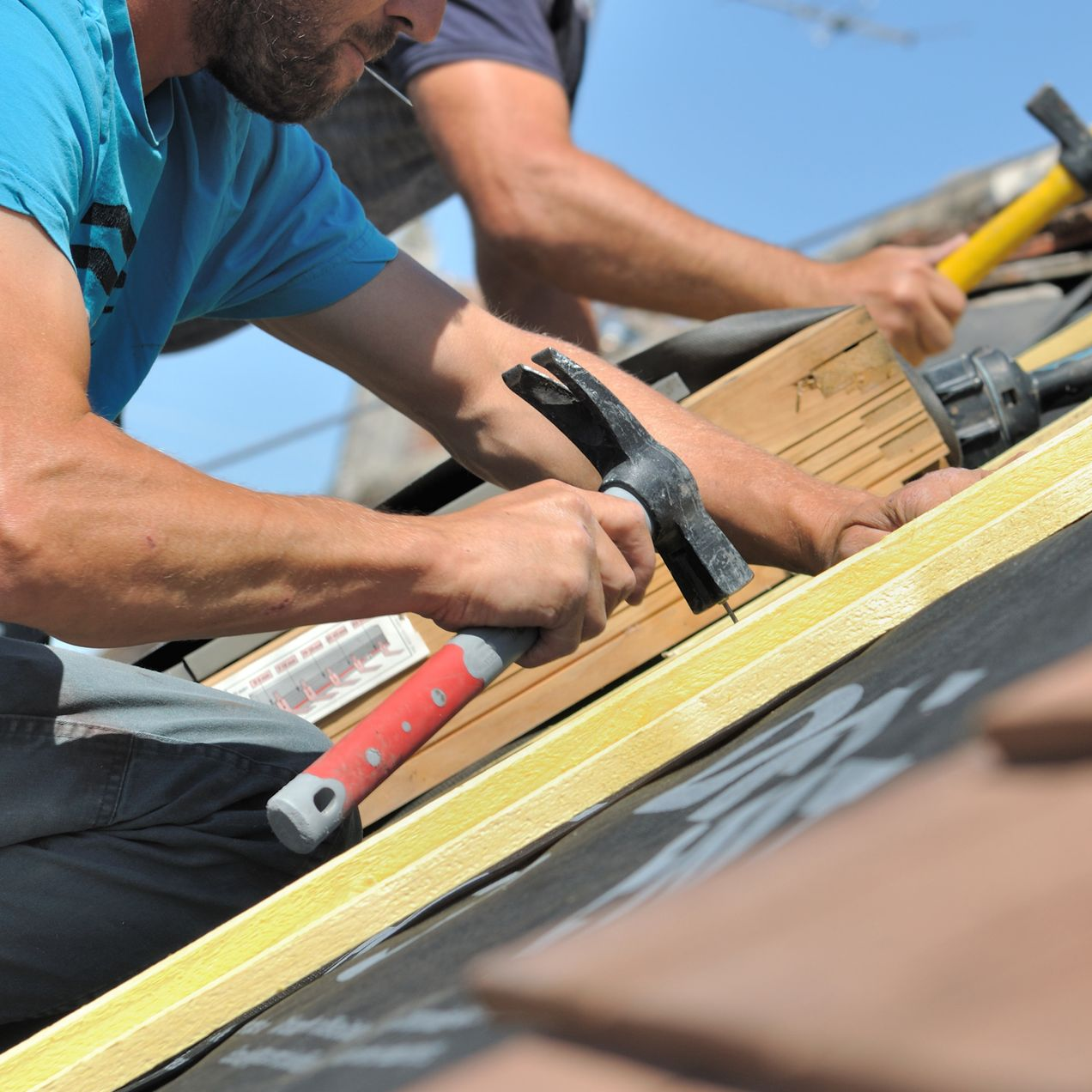 Deux couvreurs en train de réparer les éléments d'un toit au marteau