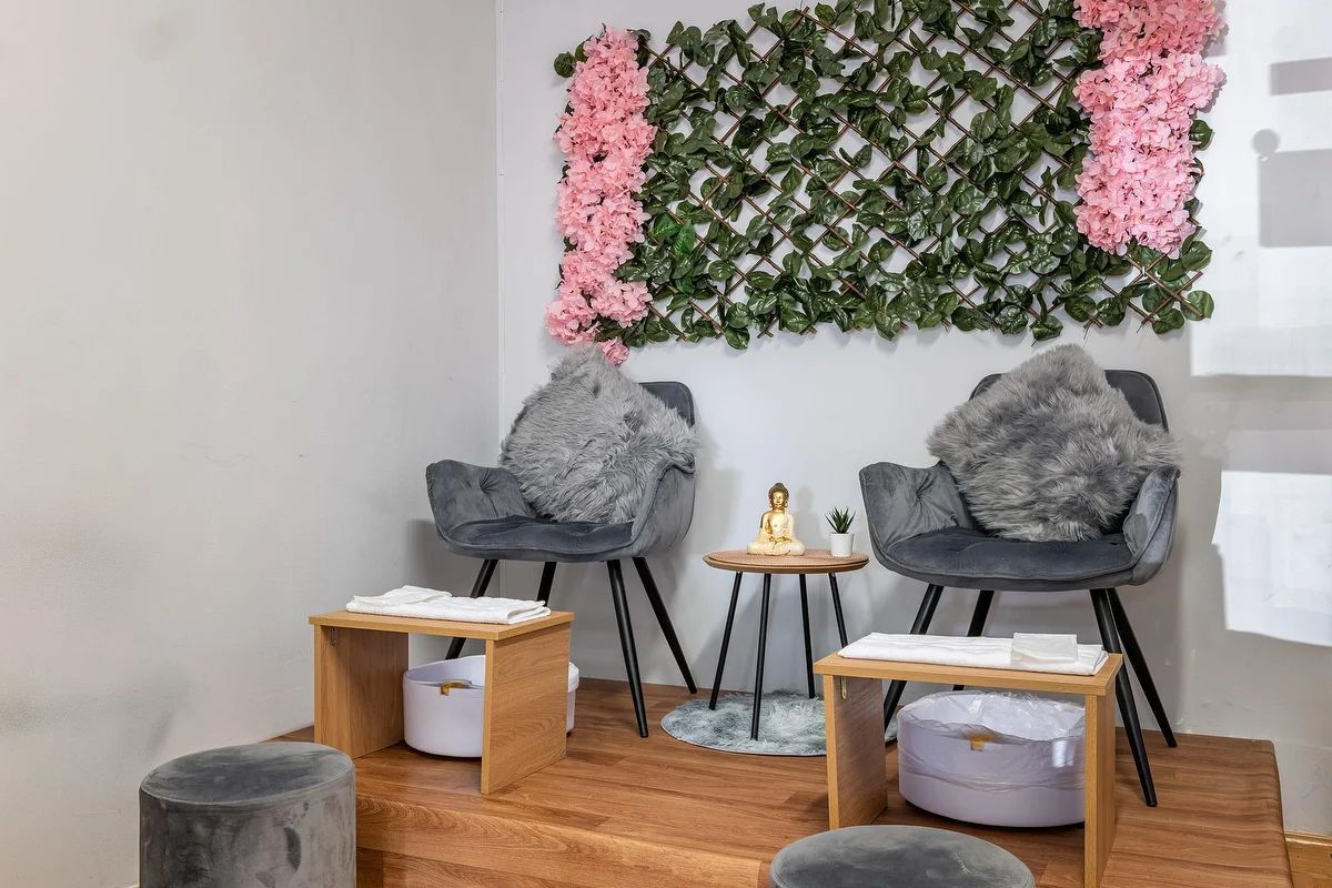 Acogedor rincón de lectura con sillas grises, mesas de madera, decoración floral en la pared y suelo de madera.