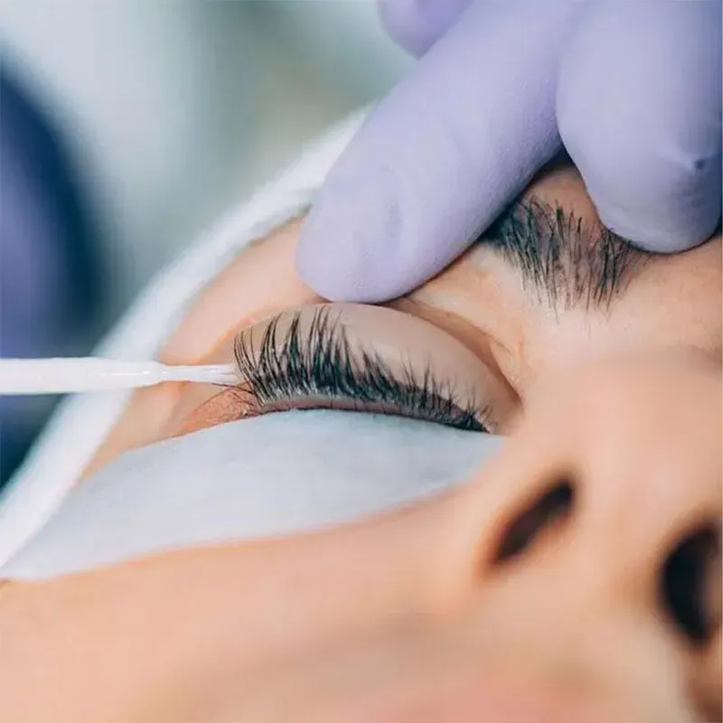 Durante un levantamiento de pestañas, una mano enguantada utiliza un aplicador de precisión