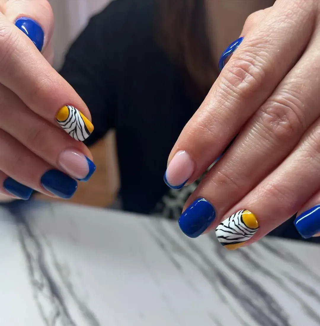 Manos con manicura azul marino, y los dedos anulares pintados con un estampado de rayas de cebra amarillas y blancas.