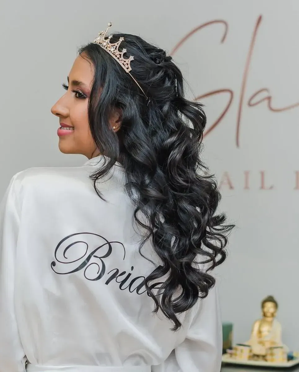 Una persona con cabello largo, oscuro y ondulado lleva una pequeña corona, de espaldas