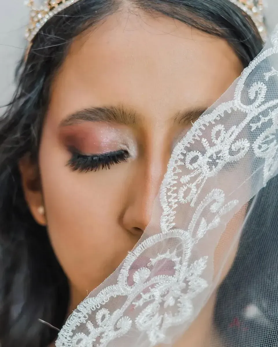 Primer plano de una persona con una corona, con los ojos cerrados y un velo de encaje blanco