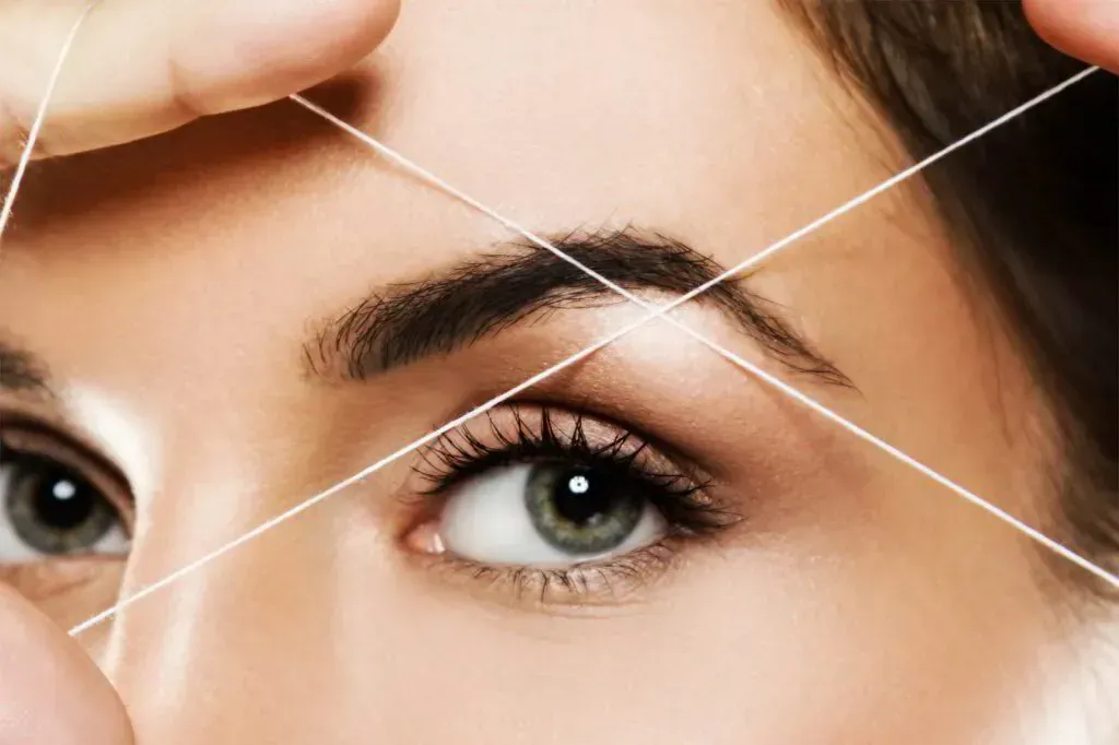 Primer plano de una persona a la que se le está depilando las cejas con hilo de algodón blanco