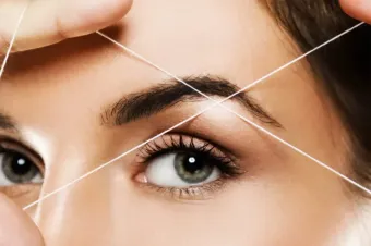 Primer plano de una persona a la que se le está depilando las cejas con hilo de algodón blanco