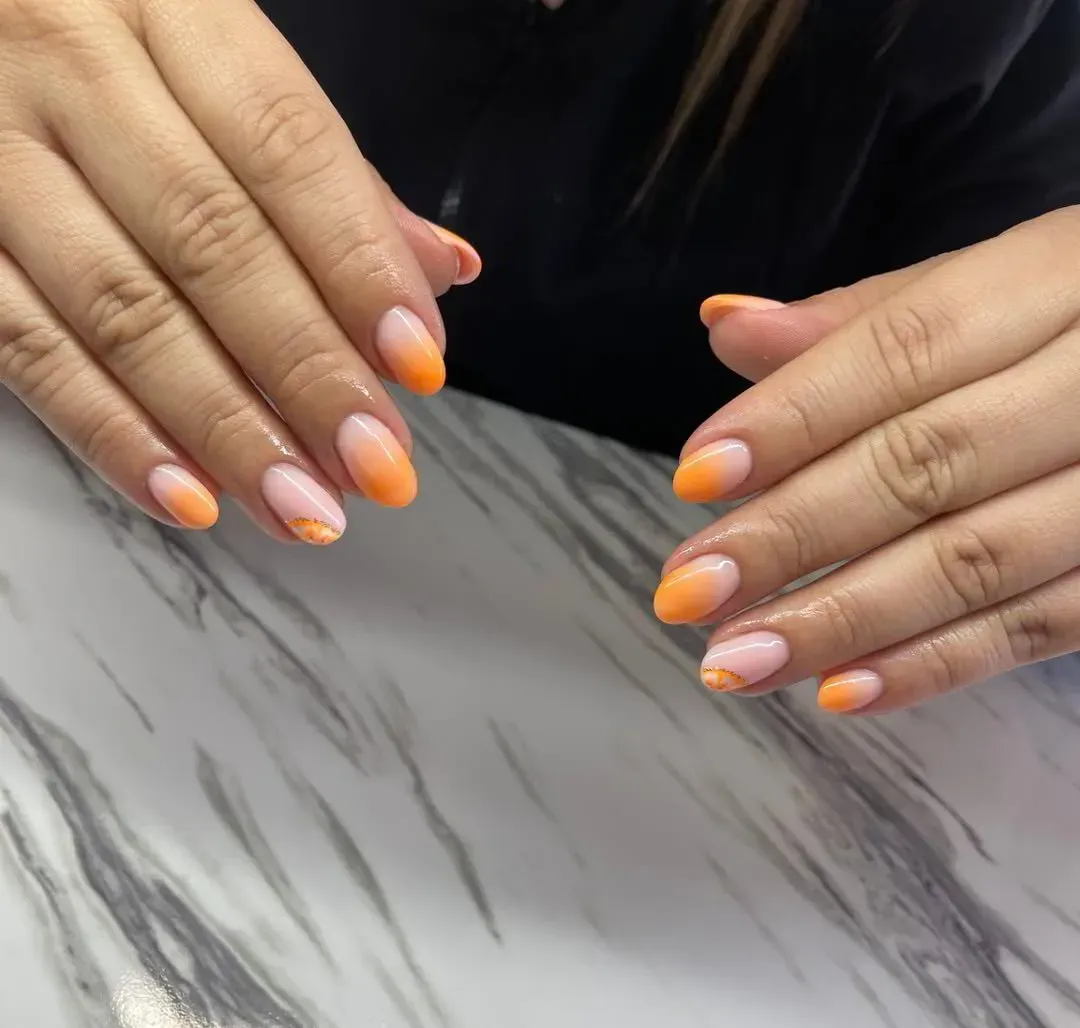 Manos bien cuidadas con uñas de forma ovalada y un diseño degradado que va del rosa claro al naranja vibrante.