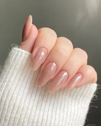 Primer plano de una mano con uñas largas en forma de almendra, pintadas de un tono nude neutro y brillante