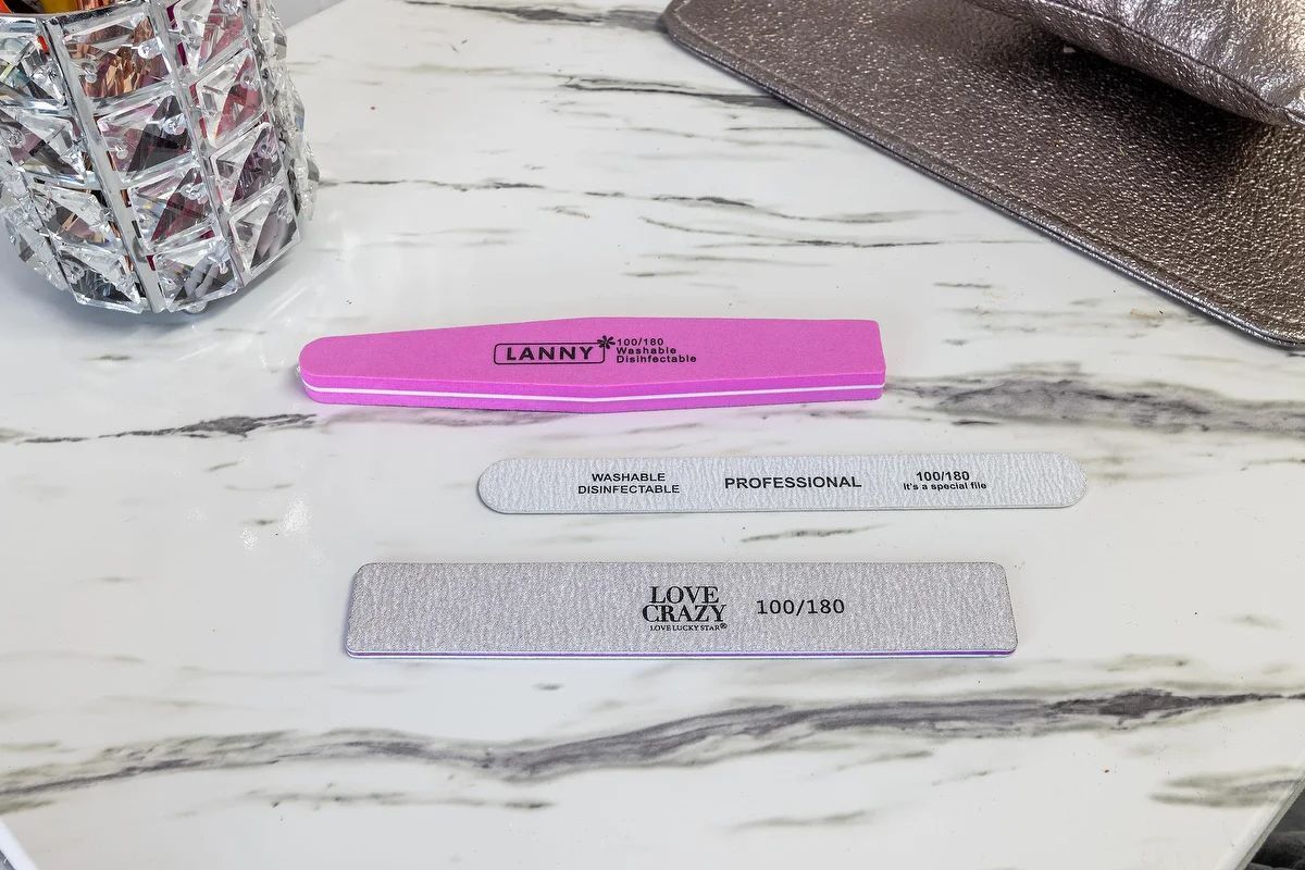 Tres limas de uñas sobre una superficie de mármol blanco, rosa, transparente y plateada brillante.
