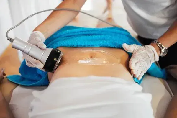 Un profesional utiliza un dispositivo portátil similar a un ecógrafo para tratar la zona abdominal de una persona