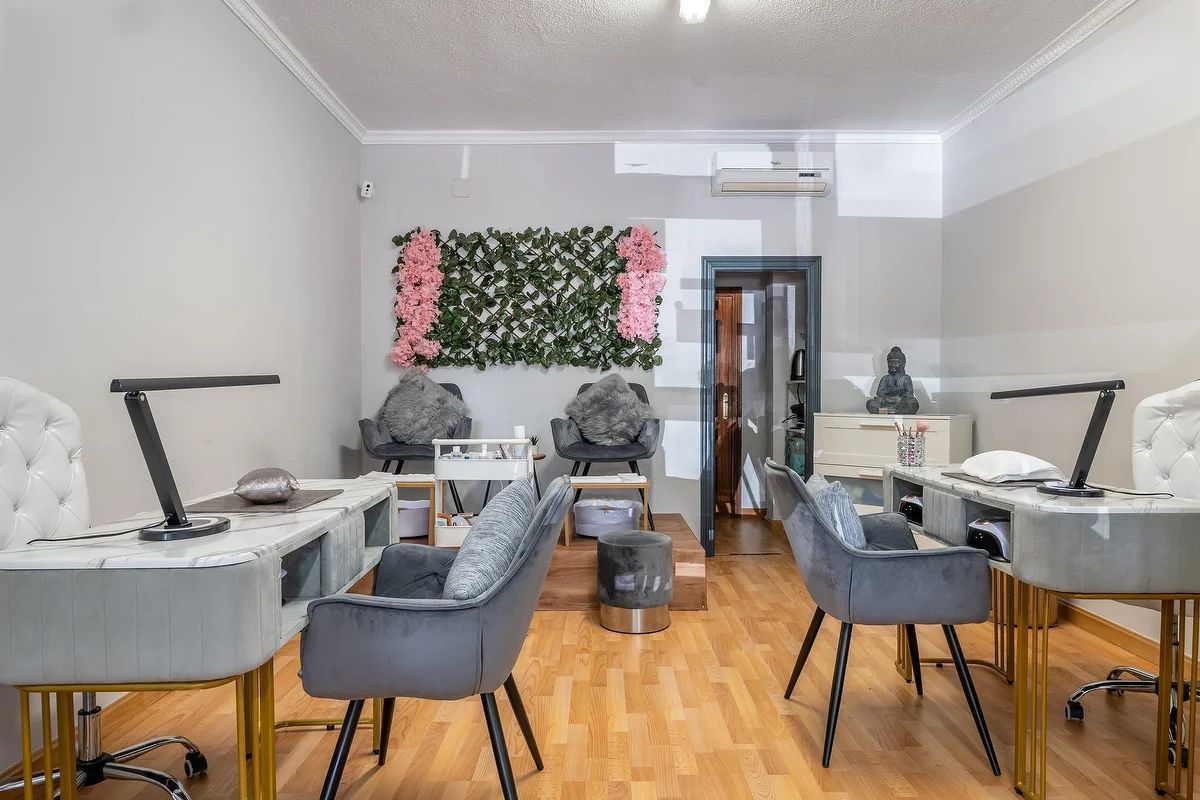 Interior del salón con mesas de manicura, sillas grises y un arreglo floral en la pared.