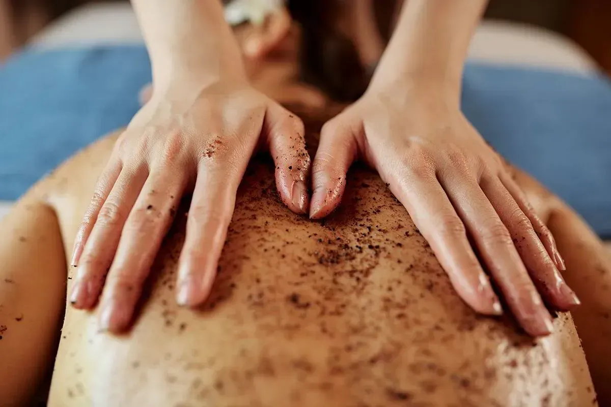Unas manos realizan un tratamiento de exfoliación de espalda a una persona tumbada en una camilla de spa