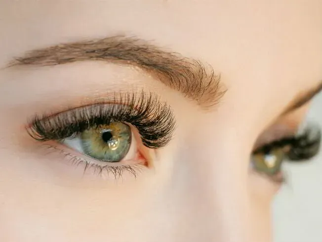 Primer plano de ojos humanos con pestañas largas y voluminosas e iris verdes, combinados con cejas bien arregladas.