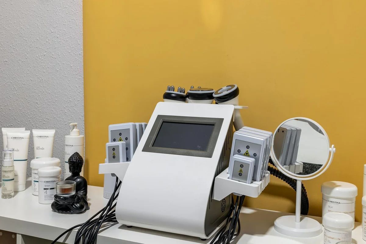 Máquina blanca para tratamientos faciales con pantalla, accesorios laterales, espejo y frascos de productos para el cuidado de la piel sobre un mostrador.