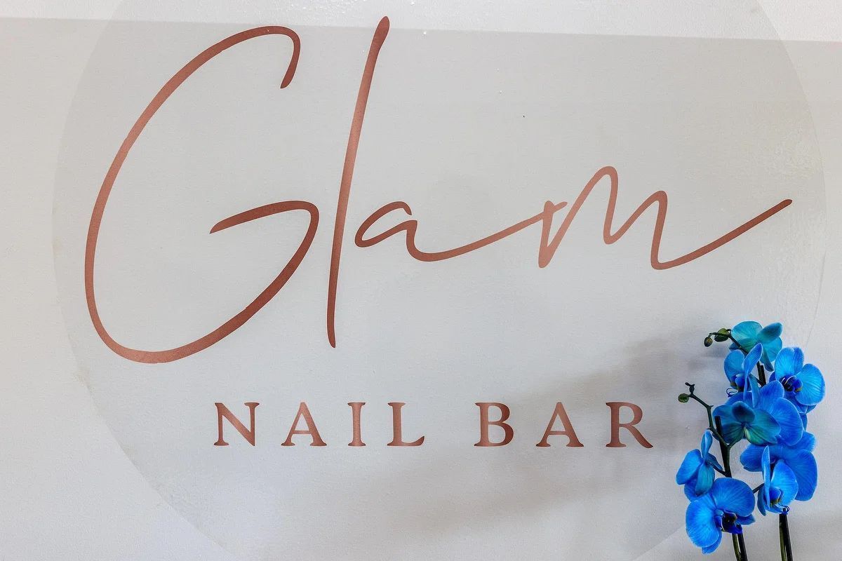 Letrero de cristal para salón de uñas con letras marrones y un detalle de flor azul.