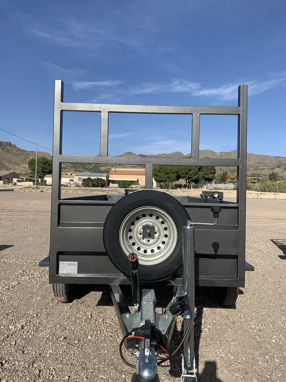 Un remolque con una llanta de repuesto adjunta está estacionado en un lote de grava.