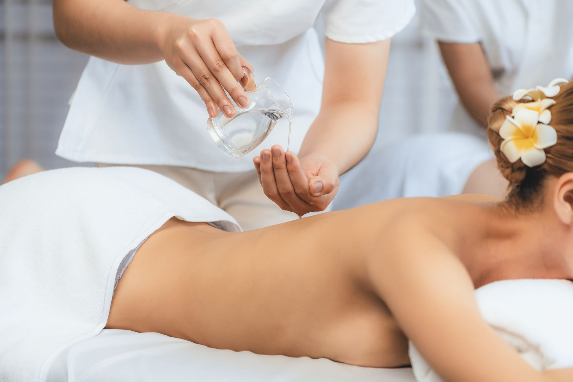 Une femme reçoit un massage tandis que le thérapeute verse de l'huile sur son dos