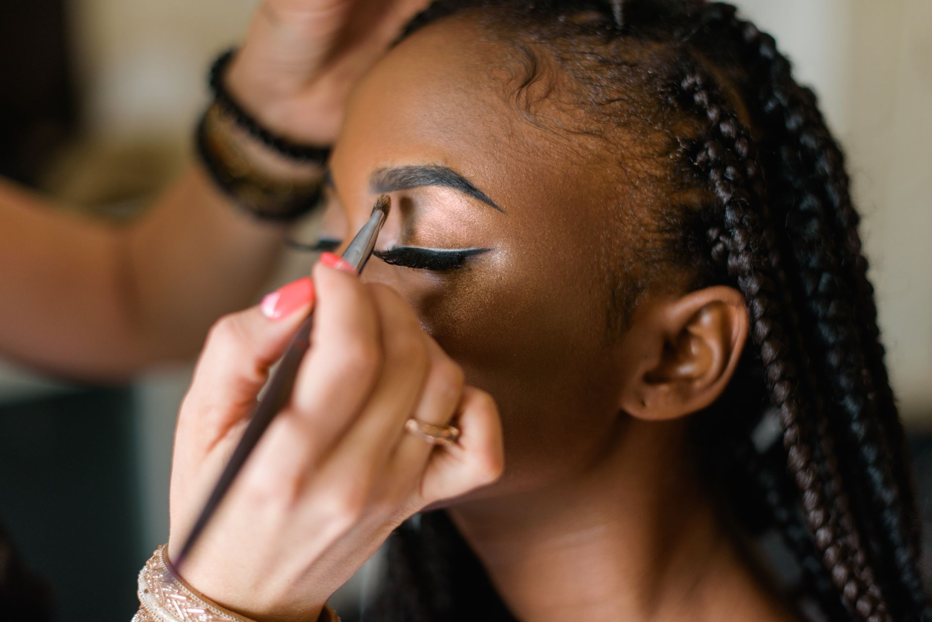 Une femme se fait maquiller les yeux, une main tien un pinceau près de la paupière.