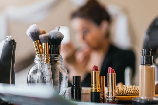 Plusieurs accessoires et outils de maquillage avec une femme en fond, floue.