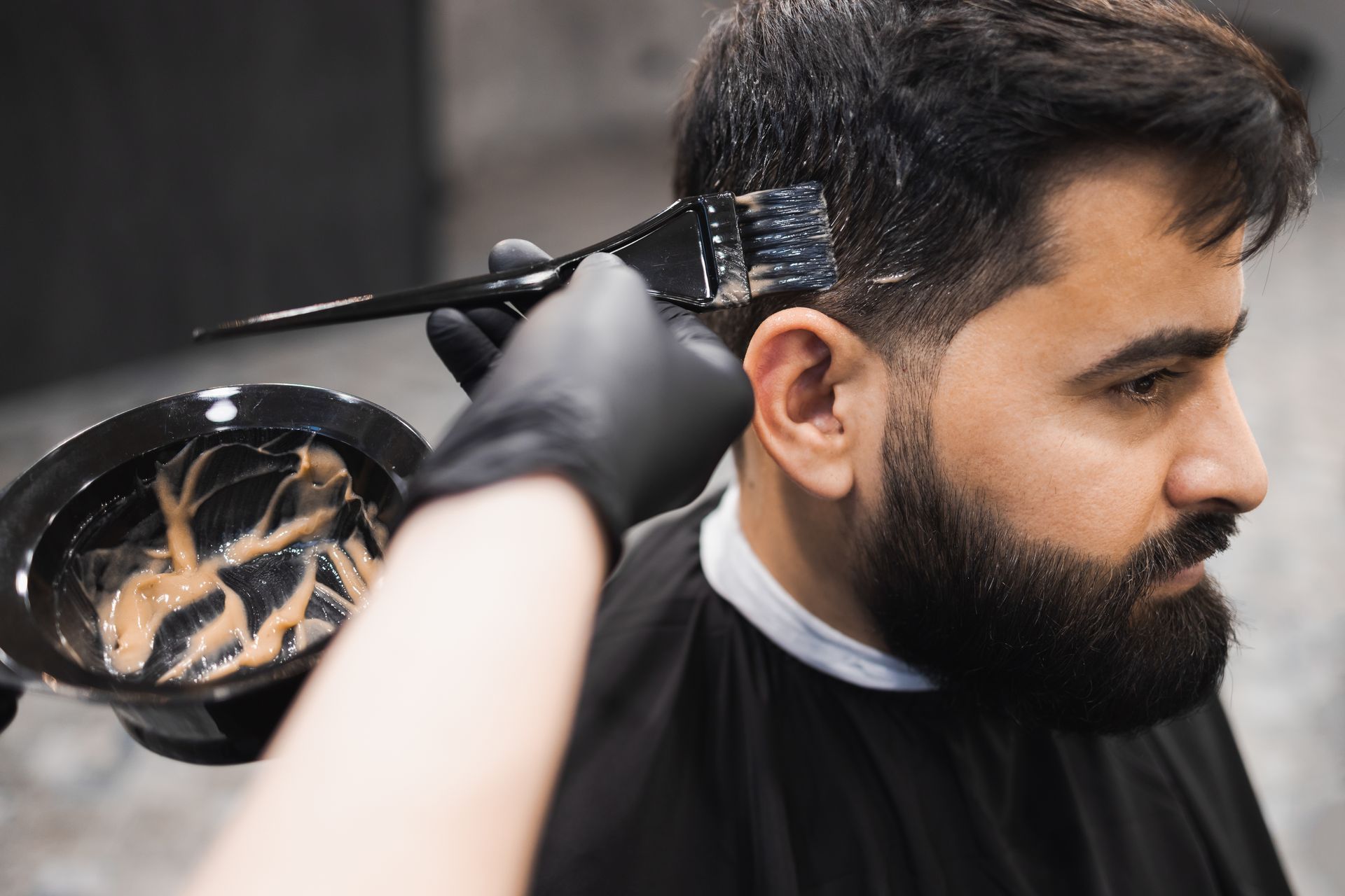 Coloration en cours de pose sur des cheveux d'un homme par une main gantée avec un pinceau.