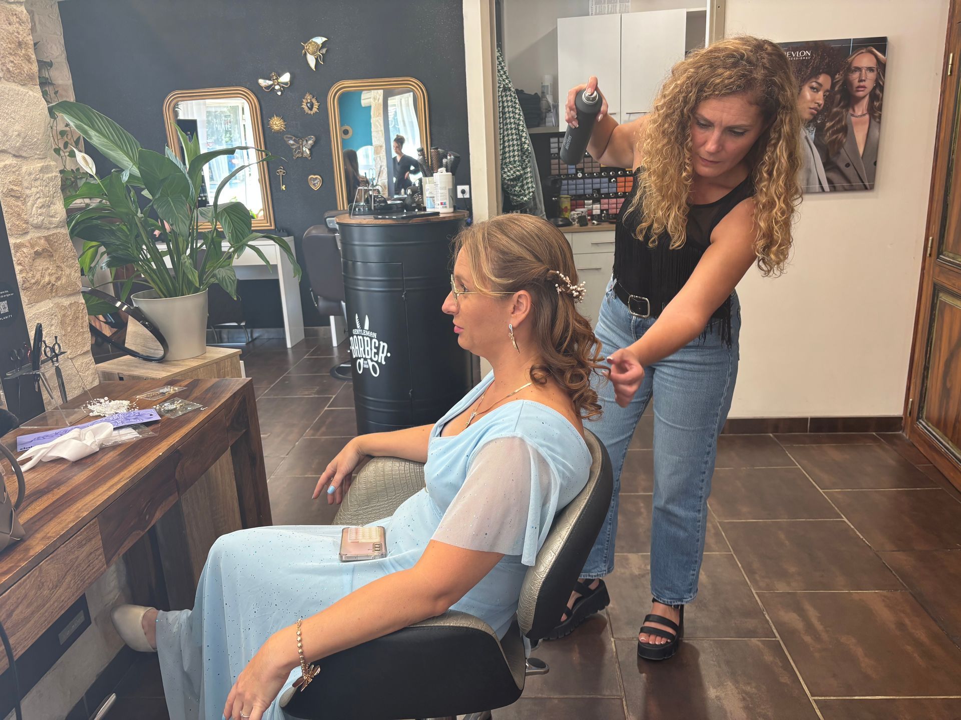 Coiffeur avec personne en tenue bleue pendant la mise en place d'une coiffure événementielle.
