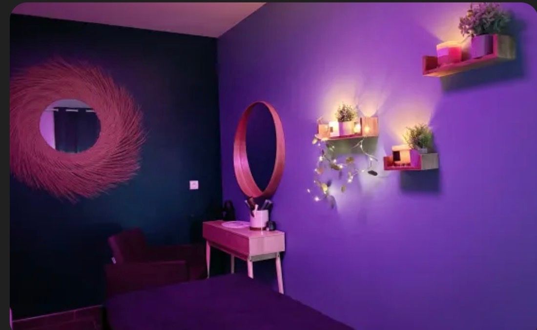 Pièce violette avec miroir, plantes et lumières sur des étagères.