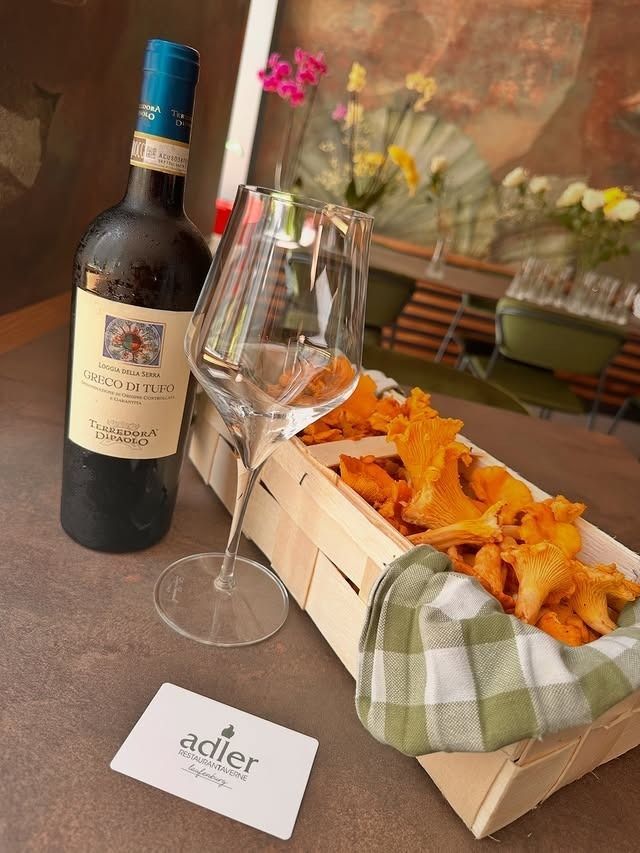 Eine Flasche Rotwein, ein Weinglas und ein Holzkorb mit Pfifferlingen auf einem Tisch mit einer Markenkarte.